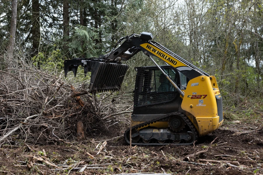 Site preparation by clearing brush using a New Holland compact track loader.