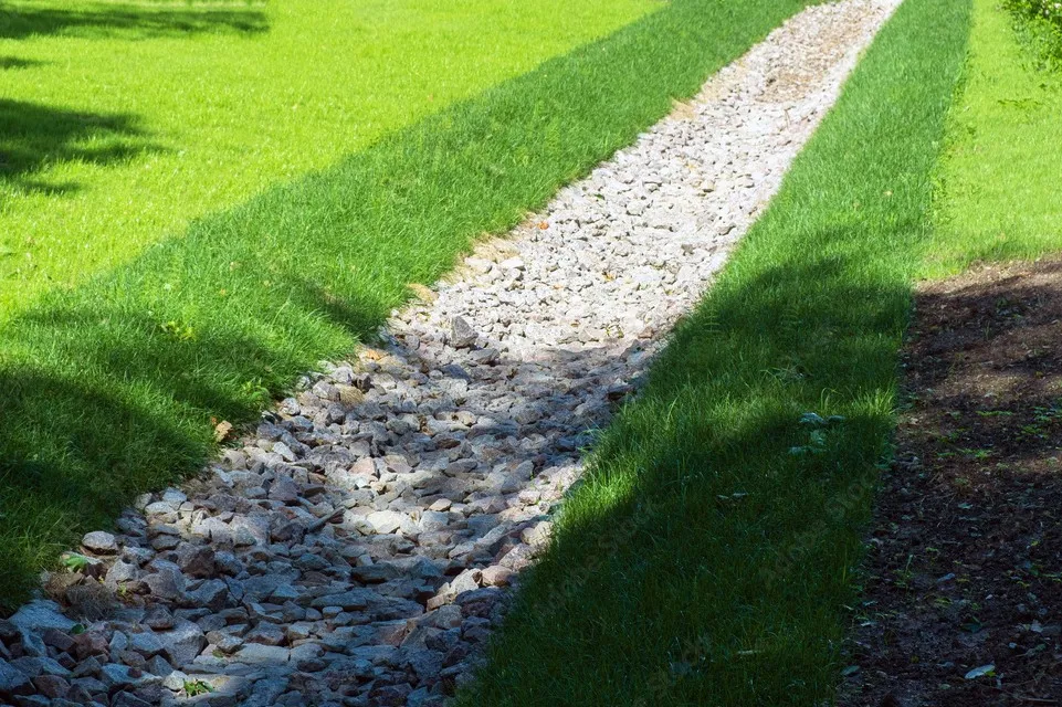 A white gravel drain installed in a green lawn.