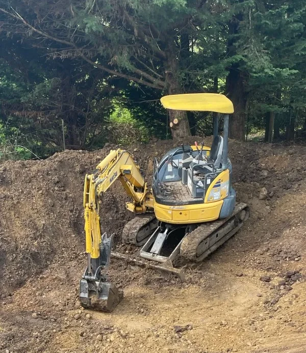 An excavator in the middle of a construction site surrounded by pine trees